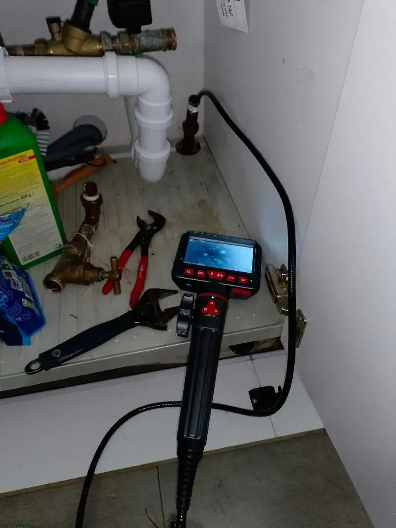 Borescope inspection camera positioned beside pipework inside a cupboard